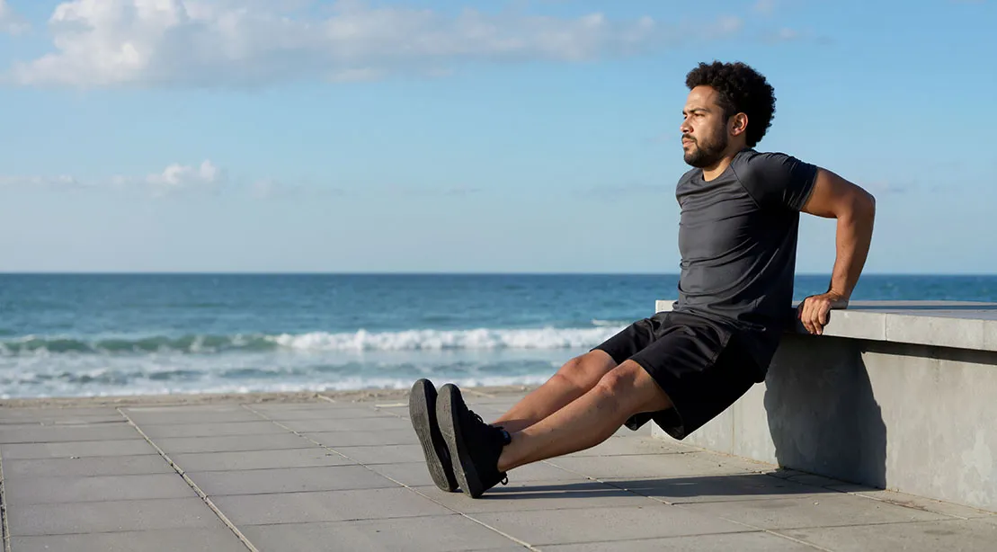 Fit man performing partial dip exercises at the beach