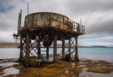AI-generated image: A heavily rusted, cylindrical metal tank sits on a concrete platform partially submerged in water.