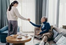 Younger woman holding hands with an older woman sitting on a sofa at home