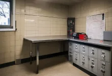 AI-generated image: A dark, tiled room contains a stainless steel table with a metal edge and several gray lockers with locks.