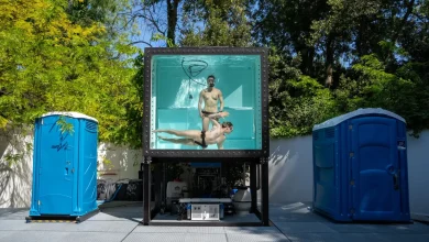 Two nude people in a dunk tank flanked by blue latrines.