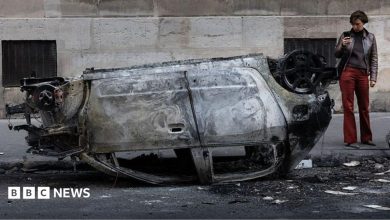 A woman takes a photo of the wreckage of a burnt-out car in central Paris
