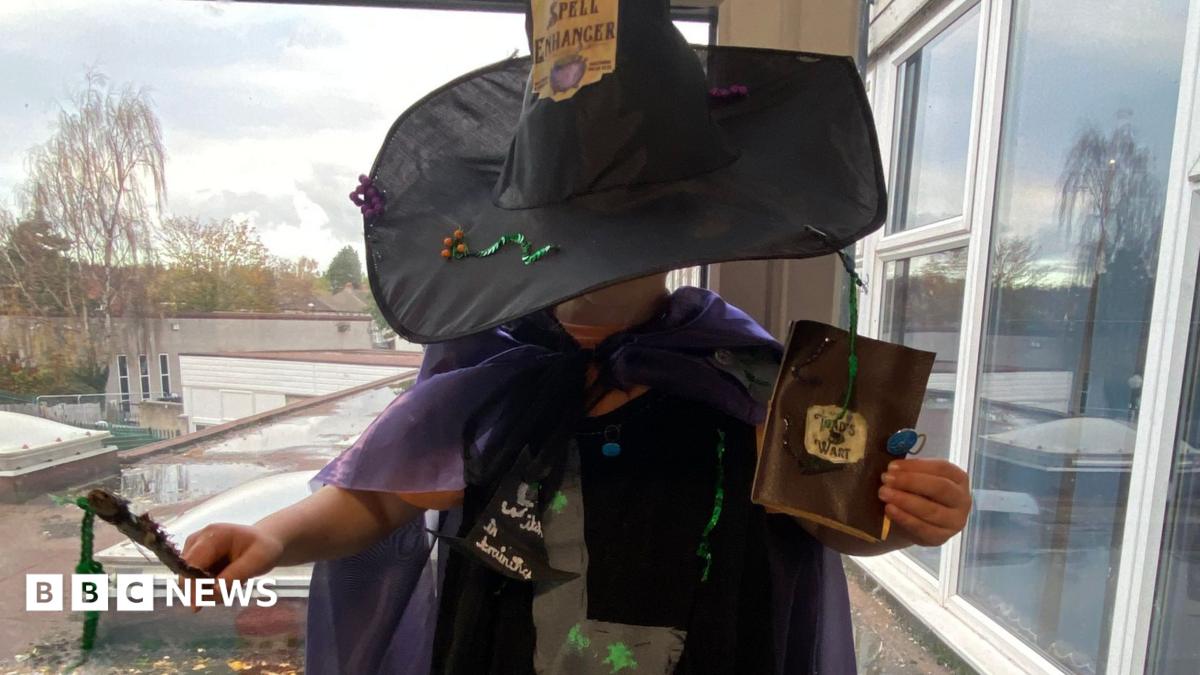 Child dressed as a witch in a homemade Halloween costume featuring a black hat, purple cape, wand and handmade accessories.