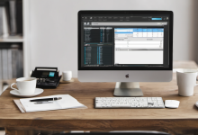 AI-generated image: A wooden desk with a silver Apple iMac computer, a white ceramic mug, a white notebook, a pen, a calculator, a mouse, and a smartphone are arranged on the desk.