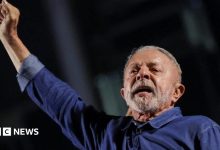 President Lula extends his right arm, his hand in a fist, as he reacts to his election. He is wearing a blue denim shirt,…