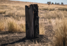 AI-generated image: A charred wooden post stands prominently in the foreground, heavily burned and broken.