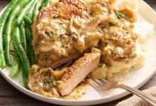 Side view of smothered pork chops on a plate with a fork and green beans.