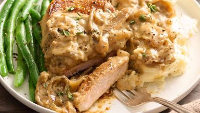 Side view of smothered pork chops on a plate with a fork and green beans.