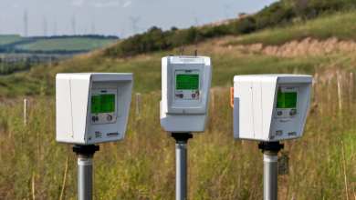 AI-generated image: Three white electronic devices with green displays are mounted on poles in a grassy field.
