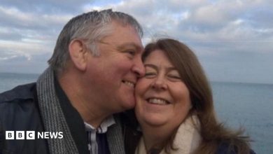 A selfie of John kissing Louisa on the cheek they are both wrapped up warm in coats and scarves and smiling as the wind…