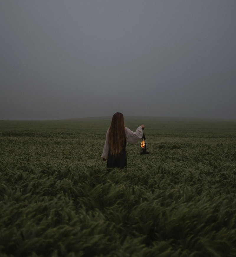 image of an outsider woman holding up a lantern in a misty landscape