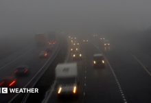 Photograph of vehicles including cars and vans on a dual carriageway road with their headlights on in foggy conditions. Other cars are attempting to…