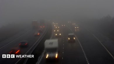 Photograph of vehicles including cars and vans on a dual carriageway road with their headlights on in foggy conditions. Other cars are attempting to…