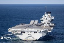 A large grey carrier is seen on the open ocean.