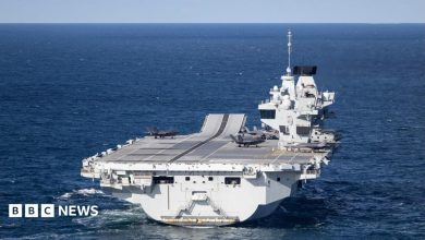 A large grey carrier is seen on the open ocean.