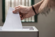 AI-generated image: A close-up shot of a hand holding a blank white paper ballot, inserting it into a gray ballot box.