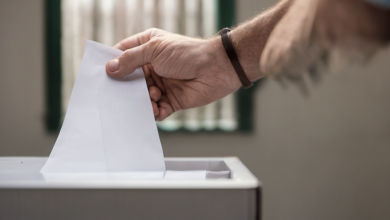 AI-generated image: A close-up shot of a hand holding a blank white paper ballot, inserting it into a gray ballot box.